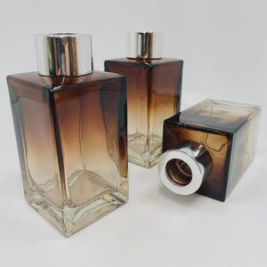 May include: Three brown glass bottles with silver tops. The bottles are rectangular with a brown to clear gradient. One bottle is lying on its side. The bottles are suitable for home fragrance.