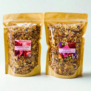 May include: Two stand-up pouches filled with dried potpourri. The left pouch features a label reading Summer Rose Pot Pourri Made With Botanical Flowers & Herbs. The right pouch features a label reading Freesia Pot Pourri Made With Botanical Flowers & Herbs.