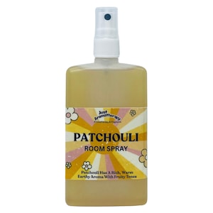 May include: A rectangular room spray bottle with a white spray nozzle. The label reads "PATCHOULI ROOM SPRAY" with text below stating "Patchouli Has A Rich, Warm Earthy Aroma With Fruity Tones". The liquid inside is yellow.