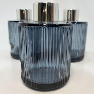 May include: Three blue glass diffuser bottles with vertical ribbed detailing. Each bottle has a silver-coloured cap. The bottles are cylindrical and have a dark blue base.