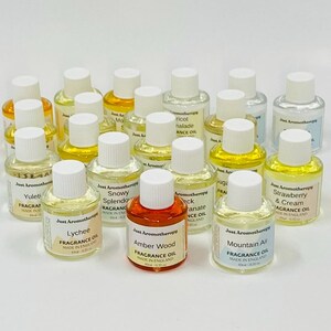 May include: A selection of small aromatherapy fragrance oil bottles with white lids and labels. The labels show scents such as "Lychee", "Amber Wood", and "Mountain Air". The bottles are displayed on a white surface.