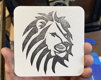 May include: A black and white lion head design printed on a white coaster.