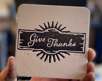 May include: A white card with a black and white stamp that says "Give Thanks" with a sunburst design.