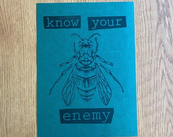 May include: A teal blue card with a black and white illustration of a wasp. The card has the text "know your enemy" in black letters.