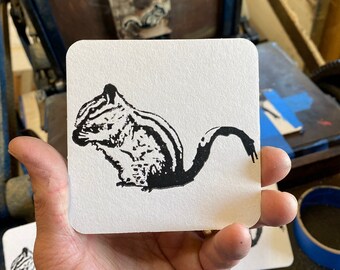 May include: A white coaster with a black and white image of a chipmunk printed on it.