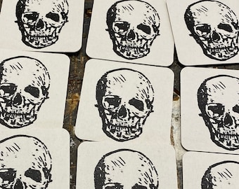 May include: A collection of square coasters with a black and white skull design printed on each coaster.