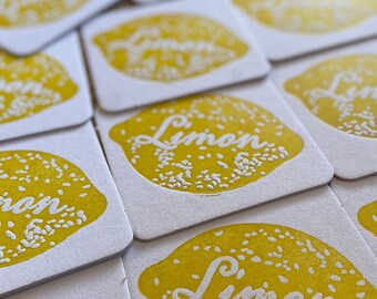 May include: A stack of white square coasters with a yellow lemon design and the word "Limon" printed in white.