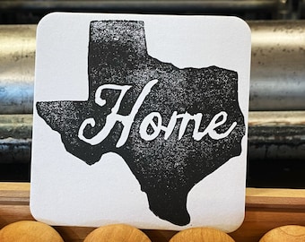 May include: A white card with a black outline of the state of Texas and the word "Home" printed in black. The card is sitting on a wooden box with four wooden stamps with brass accents.