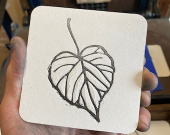May include: A black and white illustration of a leaf printed on a white coaster.