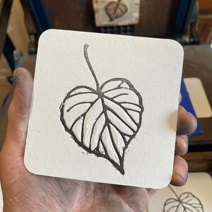 May include: A black and white illustration of a leaf printed on a white coaster.