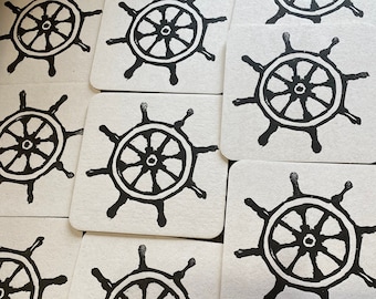 May include: A set of ten square coasters with a black and white printed design of a ship's wheel.
