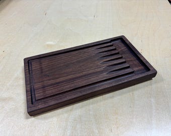 May include: A dark brown wooden cutting board with a groove for holding knives. The board is made of walnut wood and has a natural finish.