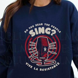 May include: A navy blue sweatshirt with a graphic of a microphone and the text "Do you hear the people sing? Vive la résistance".