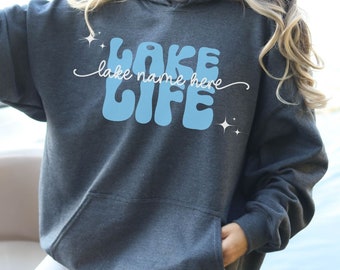 May include: A dark gray hooded sweatshirt with a light blue graphic that says "Lake Life" with the words "lake name here" written in cursive underneath.