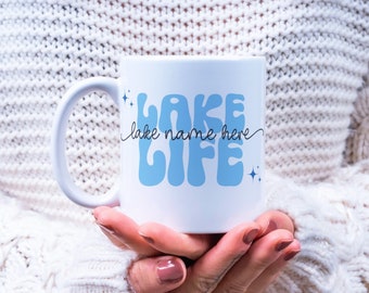 May include: White ceramic mug with a blue and white design that says "Lake Life" with the words "lake name here" written in cursive above the word "Life".