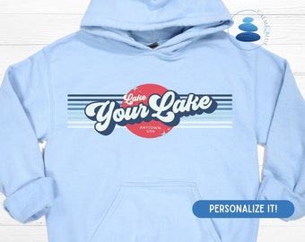 May include: Light blue hooded sweatshirt with a retro-style graphic design featuring the text "Lake Your Lake" in a red circle with white stars. The text "Anytown, USA" is printed below the circle.