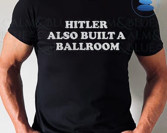 May include: Black t-shirt with the white text "HITLER ALSO BUILT A BALLROOM". The shirt has a crew neck and short sleeves. The text is in a bold, sans-serif font.