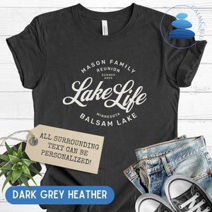 K&ouml;nnte beinhalten: Dunkelgraues T-Shirt aus Heather-Material mit wei&szlig;em Text, der "Mason Family Reunion Summer 2023 Lake Life Minnesota Balsam Lake" lautet. Der Text ist in einer Vintage-Schriftart gehalten. Ein Etikett ist am T-Shirt befestigt, auf dem "Der gesamte umgebende Text kann personalisiert werden!" steht.