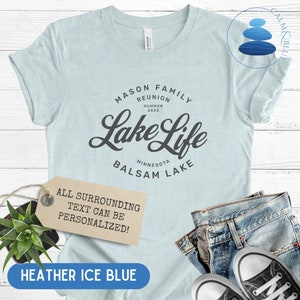 K&ouml;nnte beinhalten: Ein hellblaues T-Shirt mit dem Text "MASON FAMILY REUNION SUMMER 2023 Lake Life MINNESOTA BALSAM LAKE" in Grau. Der Text "ALL SURROUNDING TEXT CAN BE PERSONALIZED!" befindet sich auf einem braunen Etikett unter dem Shirt. Das Shirt liegt auf einer wei&szlig;en Holzoberfl&auml;che.