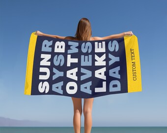 May include: A blue and white beach towel with the text "SUN SAYS  A  TW  O  A  V  E  S  L  A  K  E  D  A  Y  S" in white and blue lettering. The towel has a yellow border with the text "CUSTOM TEXT" in black lettering.
