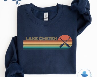 May include: Navy blue sweatshirt with a vintage-style graphic design featuring the text "LAKE CHETEK" in yellow and orange letters with a sunset and crossed paddles in the background.