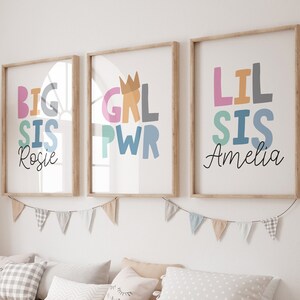 Può includere: Tre stampe incorniciate con testo colorato. La prima stampa dice "Big Sis Rosie". La seconda stampa dice "Grl Pwr". La terza stampa dice "Lil Sis Amelia".