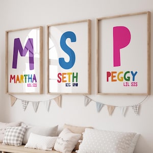May include: Three framed wall art prints featuring large colourful letters M, S, and P. The prints display the names Martha, Seth, and Peggy in multi-coloured text, along with the phrases Big Sis, Big Bro, and Lil Sis below each name.