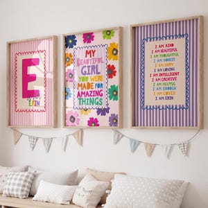 May include: Three framed wall art prints featuring colourful typography and floral patterns. The left print shows a large letter E, the centre print reads My Beautiful Girl You Were Made For Amazing Things, and the right print lists positive affirmations.
