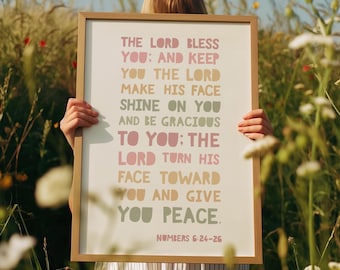 May include: A framed print with the text "THE LORD BLESS YOU: AND KEEP YOU THE LORD MAKE HIS FACE SHINE ON YOU AND BE GRACIOUS TO YOU: THE LORD TURN HIS FACE TOWARD YOU AND GIVE YOU PEACE. NUMBERS 6:24-26". The frame is light brown.