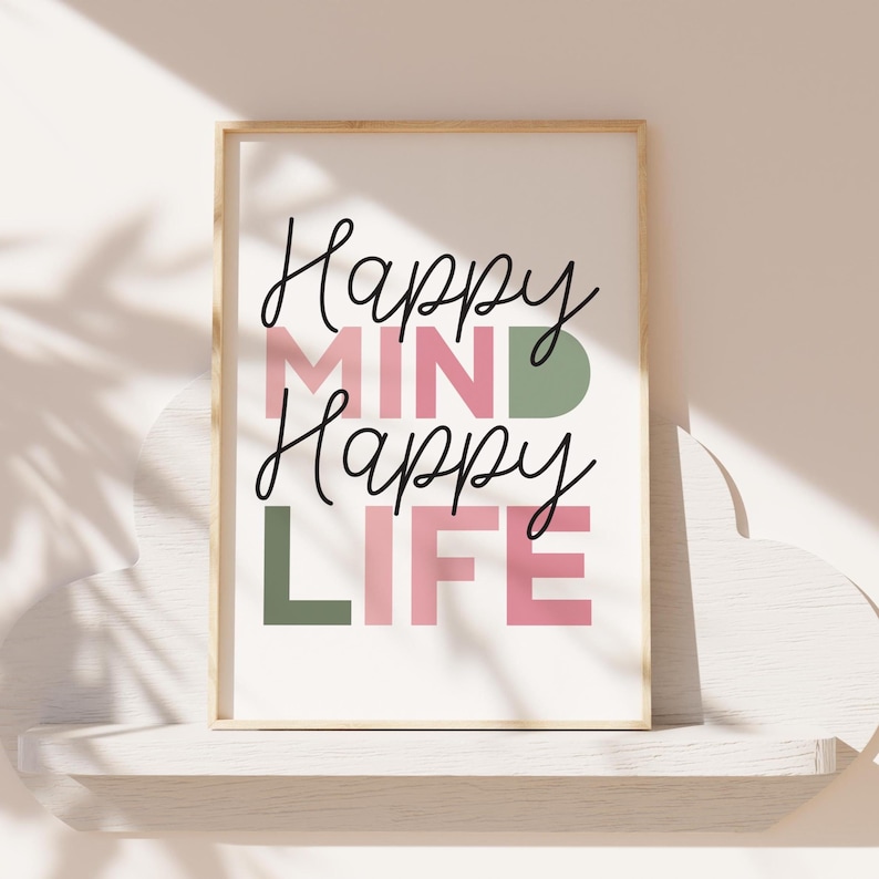 May include: A framed print with the words "Happy MIND Happy LIFE" in black script and block letters. The word "MIND" is in pink, and the "D" is green. The word "LIFE" is in pink, and the "L" is green. The frame is a light wood color.