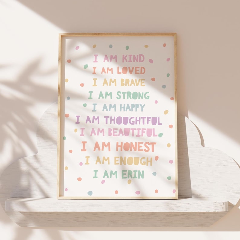 May include: A framed print with a white background and colorful polka dots. The print features a list of positive affirmations in a rainbow color scheme, including "I am kind", "I am loved", "I am brave", "I am strong", "I am happy", "I am thoughtful", "I am beautiful", "I am honest", "I am enough", and "I am Erin".