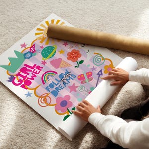 May include: A vibrant poster with the text "GIRL POWER" and "FOLLOW YOUR DREAMS" is decorated with a sun, rainbow, flowers, and other playful illustrations. A rolled-up poster and a brown cardboard tube are also present.