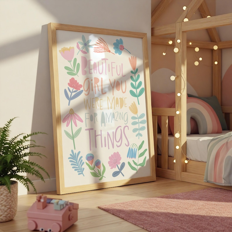 May include: A framed print with the words "BEAUTIFUL GIRL YOU WERE MADE FOR AMAZING THINGS" in colorful letters, surrounded by floral illustrations. The print is in a light wood frame, leaning against a wall in a child's room.