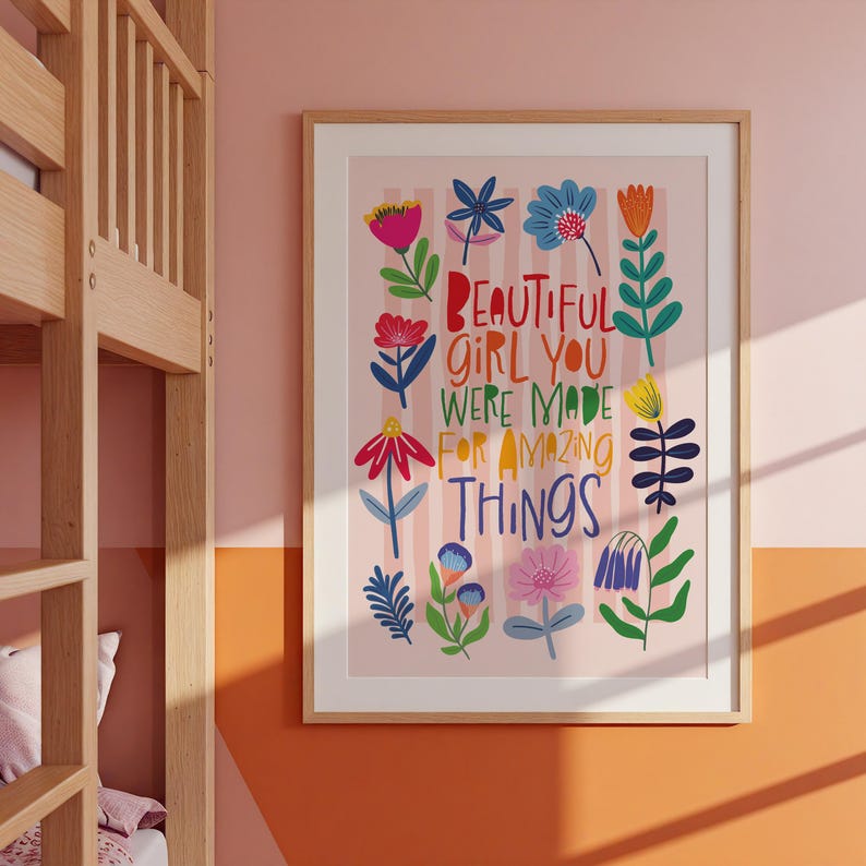 May include: A framed art print with the text "BEAUTIFUL GIRL YOU WERE MADE FOR AMAZING THINGS" surrounded by colorful floral illustrations. The print has a light pink background with vertical stripes and a wooden frame.
