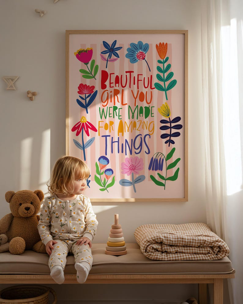 May include: A framed art print with the text "BEAUTIFUL GIRL YOU WERE MADE FOR AMAZING THINGS" in colorful letters, surrounded by floral illustrations. A child in a floral onesie sits on a bench next to a teddy bear and a wooden stacking toy.