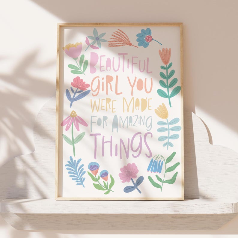 May include: A framed art print with the words "BEAUTIFUL GIRL YOU WERE MADE FOR AMAZING THINGS" in pastel colors. The print is decorated with colorful floral illustrations in pink, blue, yellow, and green. The frame is a light wood color.
