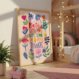 May include: A framed art print with the words "BEAUTIFUL GIRL YOU WERE MADE FOR AMAZING THINGS" in colorful letters. The print features floral illustrations in pink, red, blue, and yellow. The frame is made of light-colored wood.