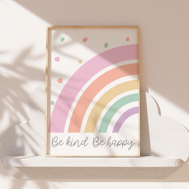 May include: A framed print with a pastel rainbow and the text "Be kind. Be happy." The rainbow is made up of pink, orange, yellow, green, and purple stripes. There are small pastel dots scattered around the rainbow.