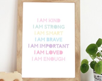 Può includere: Una stampa incorniciata con le parole "I AM KIND, I AM STRONG, I AM SMART, I AM BRAVE, I AM IMPORTANT, I AM LOVED, I AM ENOUGH" in colori pastello. La stampa è in una cornice di legno chiaro ed è esposta su una superficie bianca.