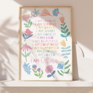 May include: A framed print with a white background featuring colorful floral illustrations and the text "I AM UNIQUE, I AM STRONG, I AM BRAVE, I AM SMART, I AM HONEST, I AM KIND, I AM BEAUTIFUL, I AM CONFIDENT, I AM SUPPORTED, I AM ENOUGH, I AM LOVED, I AM Olivia."