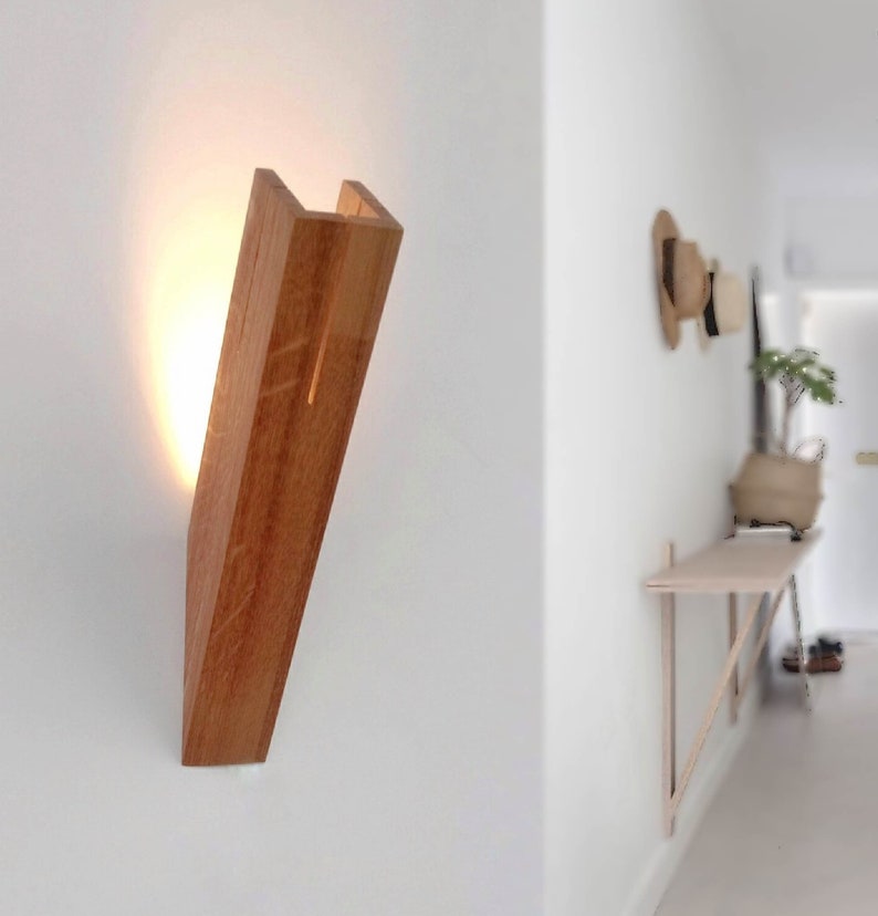 May include: A wooden wall-mounted light fixture with a warm light emanating from the top. The fixture is angled slightly and has a natural wood finish.
