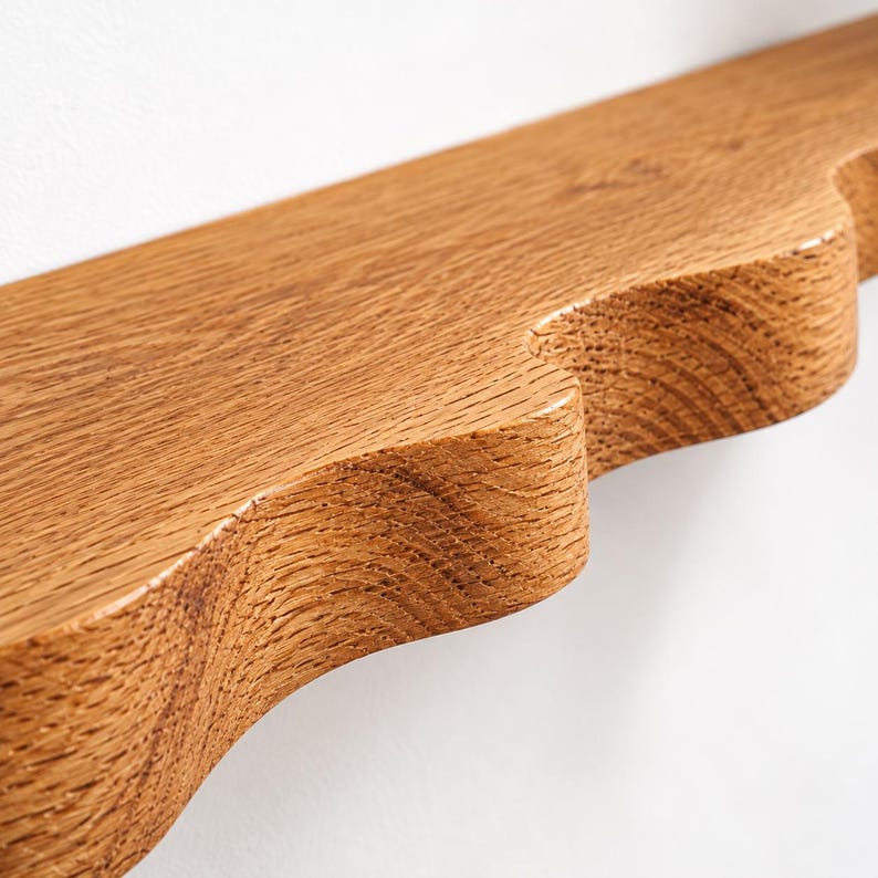 May include: A light brown wooden shelf featuring a distinct scalloped edge design. The surface displays a visible natural wood grain pattern with a smooth finish, highlighting the texture and warm tones of the timber material.