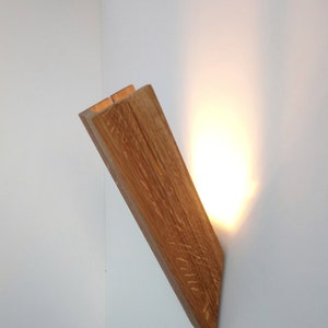 May include: A wooden wall sconce with a warm light emanating from the top. The sconce is made of natural wood with a rustic finish.