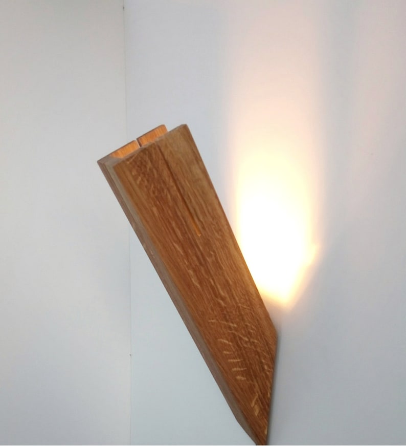 May include: A wooden wall sconce with a warm light emanating from the top. The sconce is made of natural wood with a rustic finish.