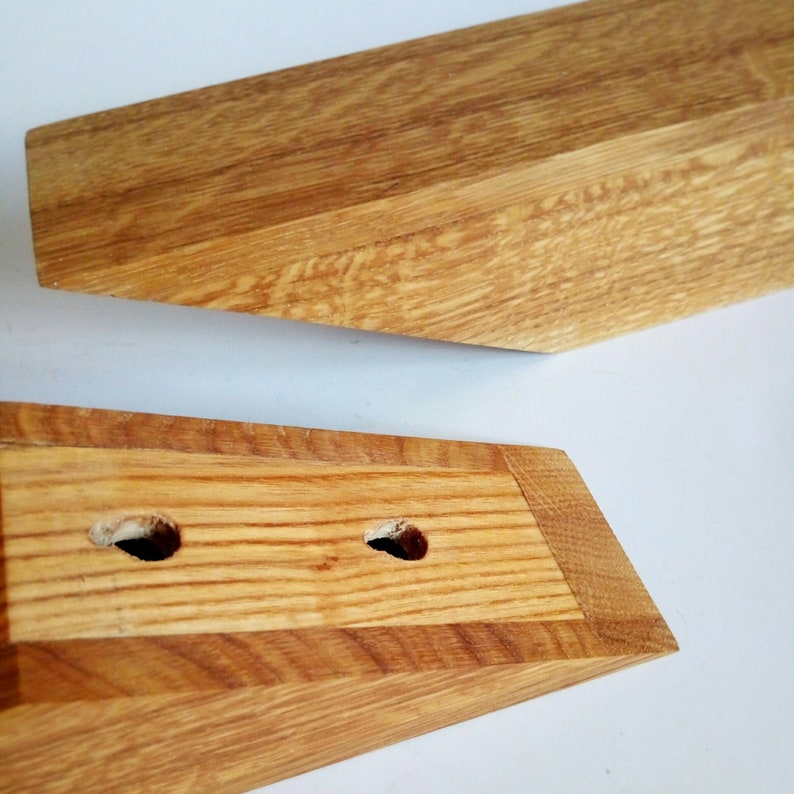 May include: Two wooden pieces of furniture with a natural wood finish. The top piece is a long, thin, rectangular shape with a slightly angled edge. The bottom piece is a shorter, wider, rectangular shape with two holes drilled in the top.