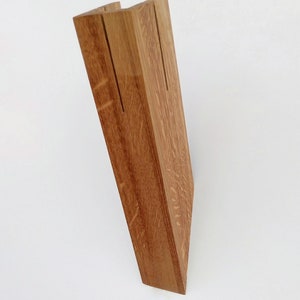 May include: A wooden stand with two slots for holding items, such as cards or photos. The stand is made of natural wood with a light brown color.