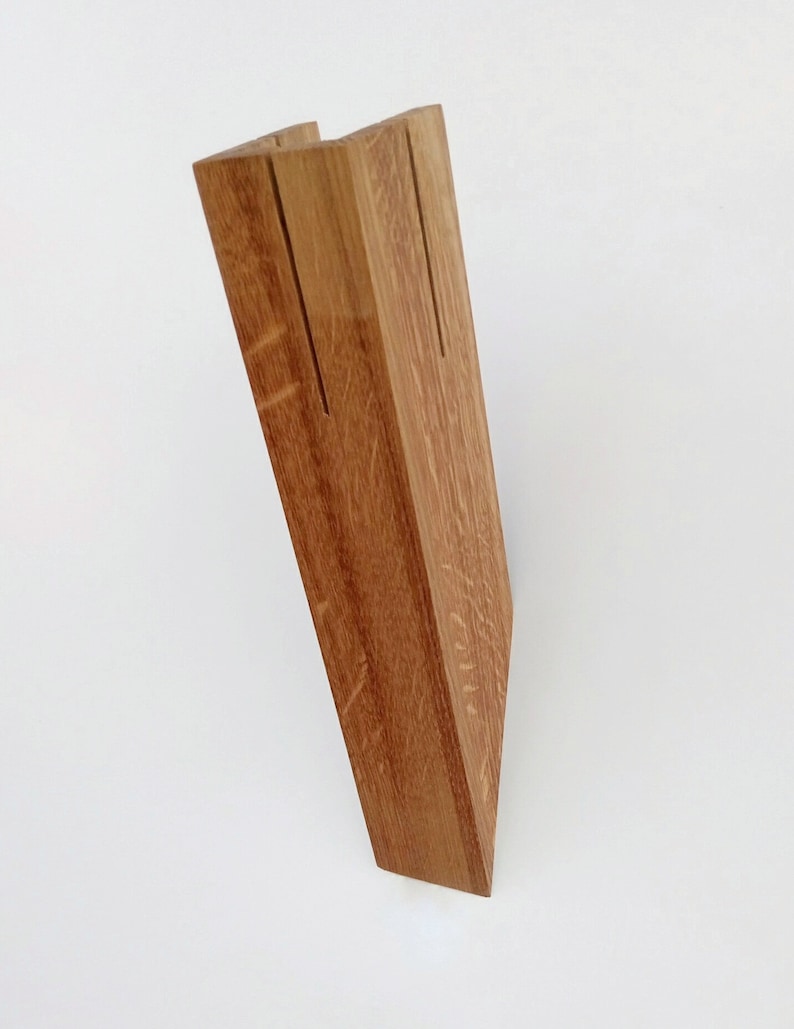 May include: A wooden stand with two slots for holding items, such as cards or photos. The stand is made of natural wood with a light brown color.