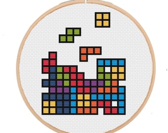 May include: A colorful cross-stitch pattern of Tetris blocks in a hoop. The blocks are arranged in a random pattern, with some blocks falling from the top of the hoop.