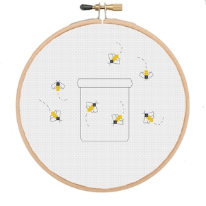Può includere: Un cerchio da ricamo bianco con un disegno a punto croce di un barattolo di miele e api. Le api sono gialle e nere e volano intorno al barattolo.