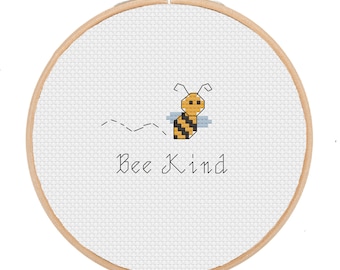 Può includere: Un cerchio da ricamo bianco con un disegno di ape giallo e nero e il testo "Bee Kind".